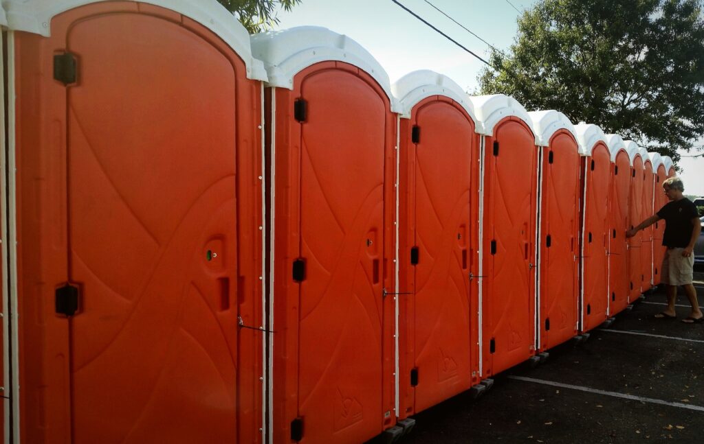 Orange outdoor bathrooms for use at outdoor event stand tall all in a row as senior enters one.